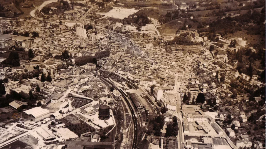Vue aérienne de Voiron vers 1970 depuis le sud-est ; les usines à gauche, le quartier de la gare, la ville médiévale à droite, le boulevard Jules-Ravat en haut à gauche (AM Voiron). © Archives municipales de Voiron