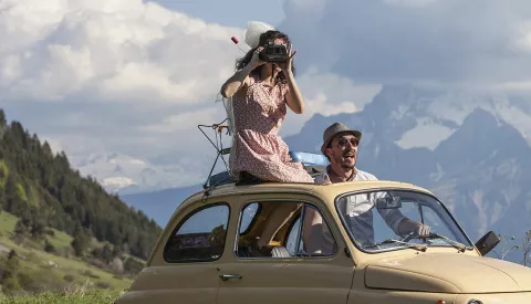 un homme et une femme dans une coccinelle décapotée sur fond de montagne © Jean-Pierre Angéi